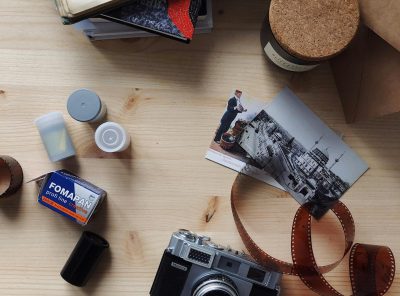 A flatlay of vintage camera, film rolls, and photographs on a wooden table.