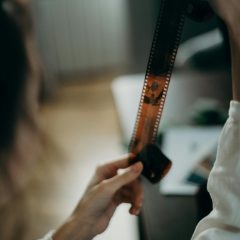 A person carefully examines a 35mm film strip in a cozy indoor setting, showcasing film photography nostalgia.
