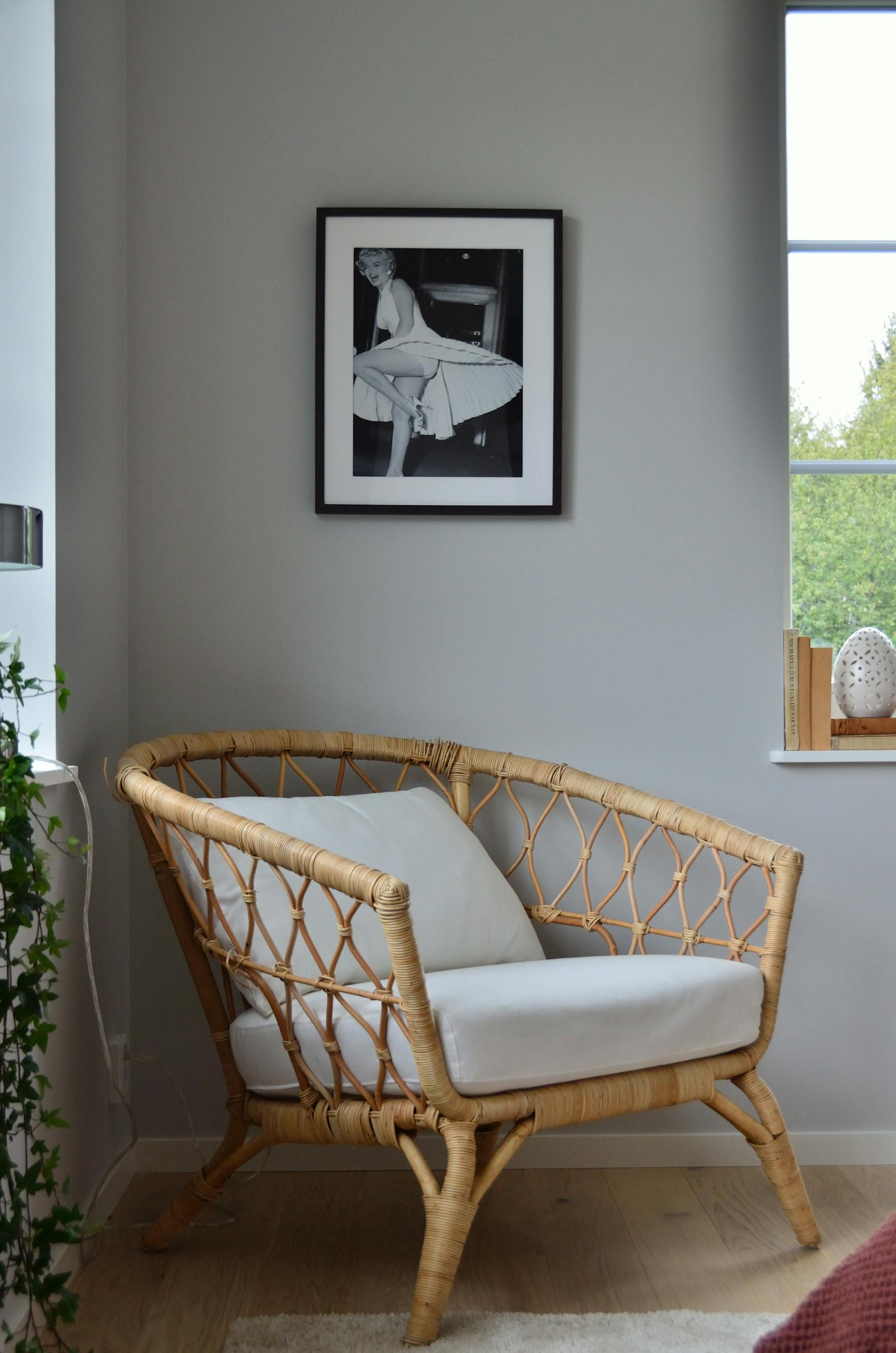 A stylish wicker chair in a Scandinavian-designed room with a framed photo on the wall.
